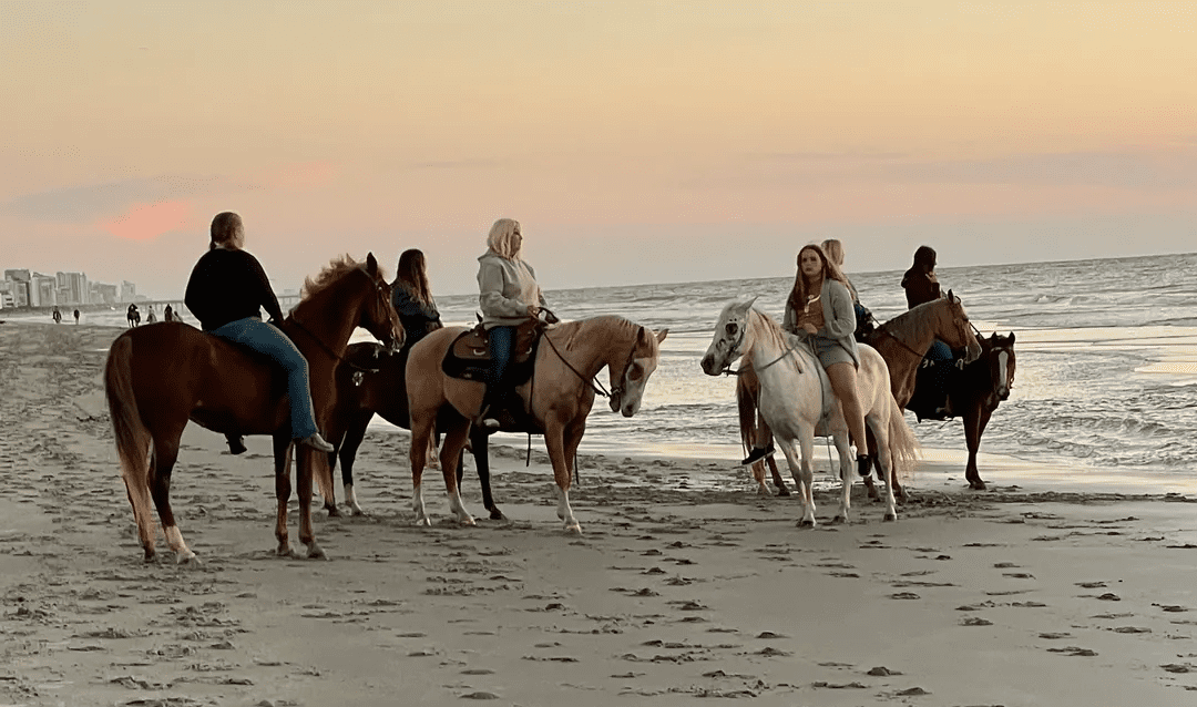 A group of people riding horses on the beach.